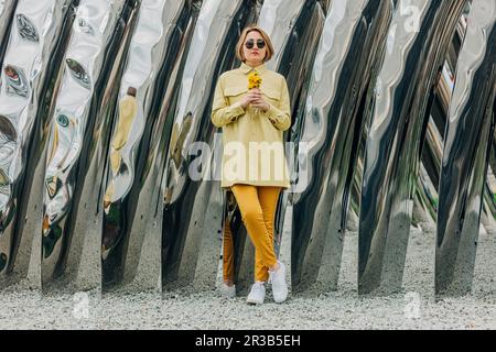 Woman holding dandelions in front of metal structure Stock Photo