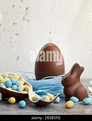 Easter chocolate egg in a blueberry candy nest, and a chocolate bunny, and a halved chocolate egg filled with mini chocolate eggs Stock Photo