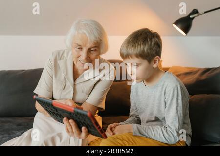 Grandmother and grandson watching video on tablet PC sitting at home Stock Photo
