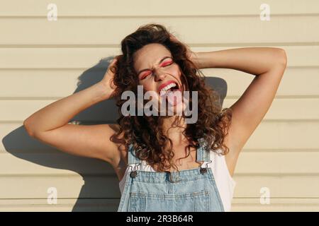Carefree woman sticking out tongue in front of wall Stock Photo