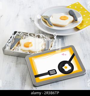 Fried egg and cutlery biscuits in a tin and on a plate Stock Photo