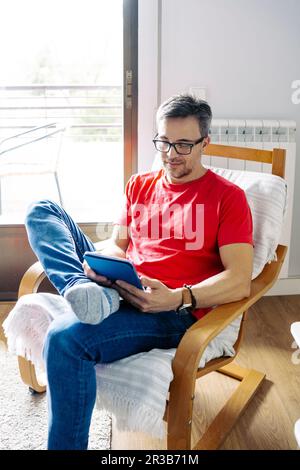 Man using tablet PC sitting on chair at home Stock Photo
