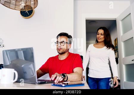 Man working on laptop with woman standing behind at home Stock Photo