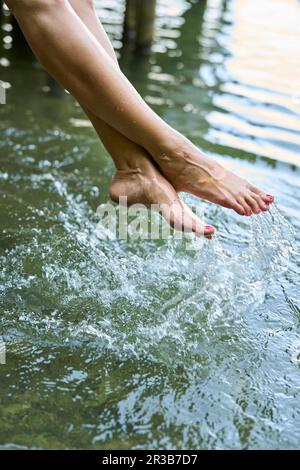 Woman splashing water with feet in lake Stock Photo