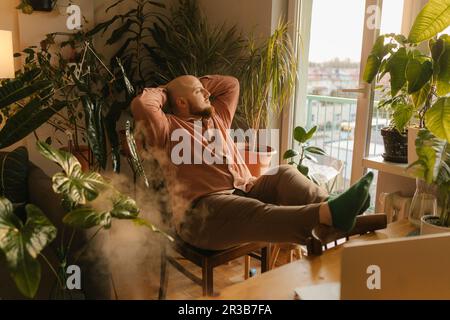 Man sitting with hands behind head on chair at home Stock Photo