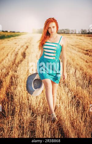 Red hair girl enjoying nature in meadow. Beautiful woman in blue dress walking on the bevelled, Sun Stock Photo