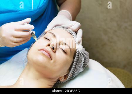 Beautician performs a needle mesotherapy treatment on a woman's face Stock Photo