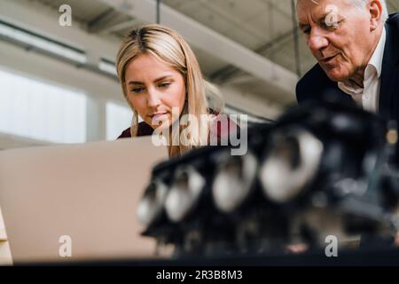 Focused businesswoman using laptop by businessman in factory Stock Photo