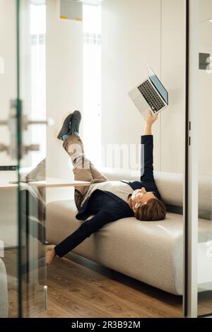 Businessman holding laptop lying on couch in lounge room Stock Photo