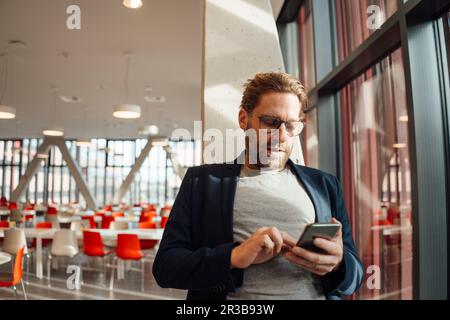 Businessman text messaging through smart phone at cafeteria Stock Photo