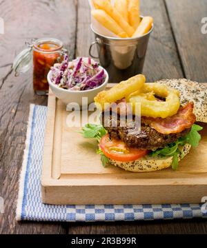 Home made burger with rocket lettuce, tomato, bacon and onion rings in a sesame seed bun Stock Photo
