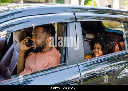 Father talking on smart phone with daughter sitting in car Stock Photo