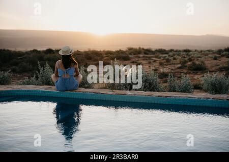 Woman looking at sunset sitting on poolside Stock Photo