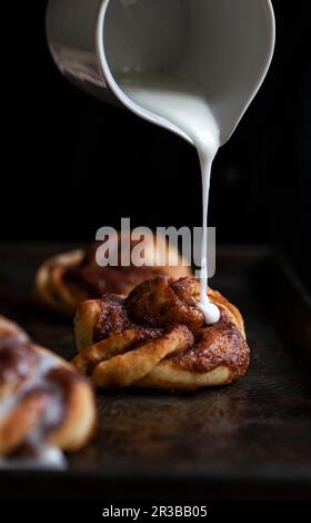 A cinnamon bun on a baking sheet being drizzled with icing Stock Photo