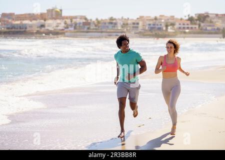 Smiling couple jogging together at beach Stock Photo