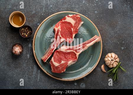Two raw marbled Tomahawk meat steaks with herbs and seasonings Stock Photo