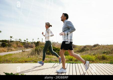 Mature couple running on boardwalk at beach Stock Photo