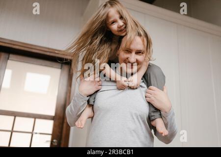 Smiling father carrying daughter on shoulders at home Stock Photo