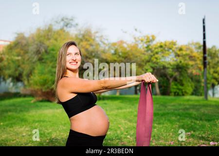 Smiling pregnant woman exercising with resistance band on lawn Stock Photo