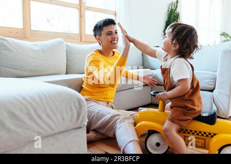 Mother giving high-five to son sitting on toy car at home Stock Photo