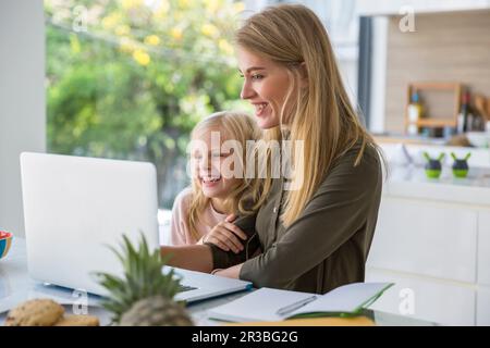 Happy woman using laptop by daughter at home Stock Photo