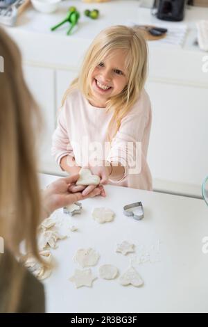 Happy daughter showing heart shape made from dough to mother at home Stock Photo