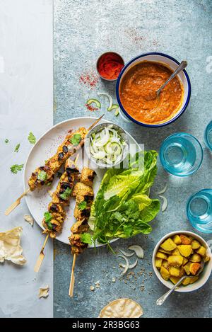 Chicken tikka skewers with masala sauce, bombay potatoes, pickled onion and cucumber salad and crunchy lettuce Stock Photo