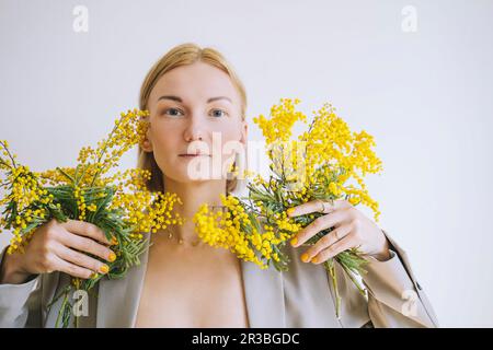 Blond woman holding bunch of mimosa flowers against white background Stock Photo