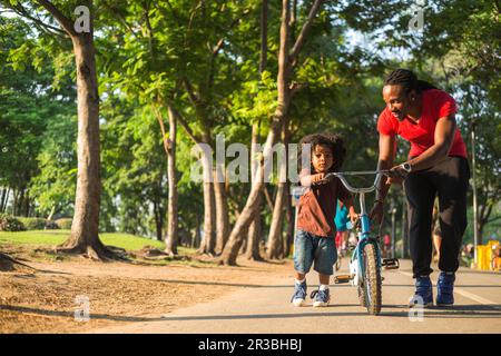 Father wheeling bicycle with son on footpath at park Stock Photo