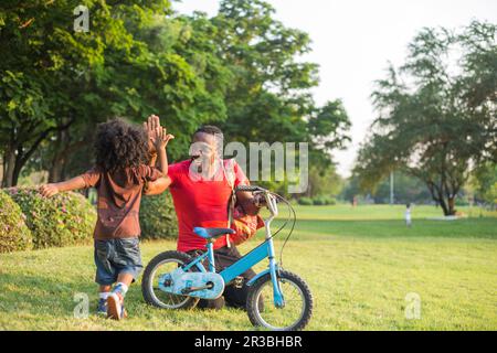 Father giving high-five to son by bicycle at park Stock Photo