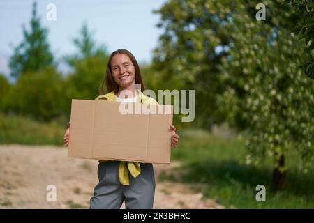 Smiling woman holding blank cardboard cut out in garden Stock Photo