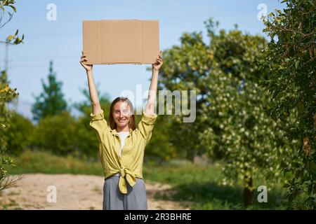 Smiling woman holding cardboard cut out with arms raised in garden Stock Photo