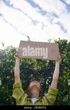 Woman holding cardboard cut out with Save The Planet text near tree in garden Stock Photo