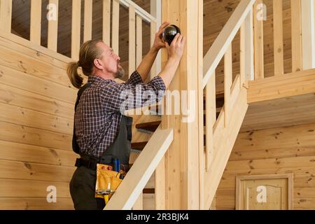 Side view of mature male worker of household service company in workwear installing alarm system on wooden pile over staircase Stock Photo