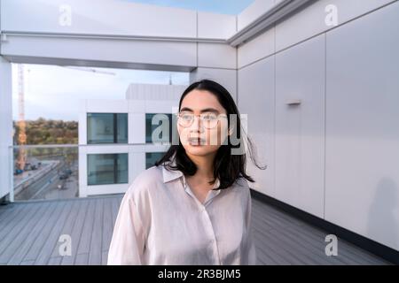 Thoughtful young businesswoman in white shirt on terrace of office building Stock Photo