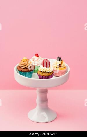 Assorted mini cupcakes on a cake stand against a pink background Stock Photo