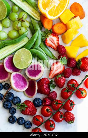 Various fruits and vegetables, arranged by colour on a marble countertop Stock Photo