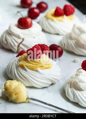 Individual meringues topped with lemon curd, raspberries, whipped cream and cherries Stock Photo