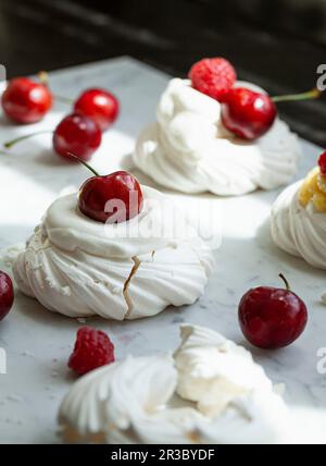 Individual meringues topped with raspberries, whipped cream and cherries Stock Photo