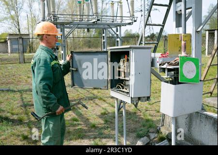 At the power substation. Worker checking connections on the electric board turning start tumbler Stock Photo