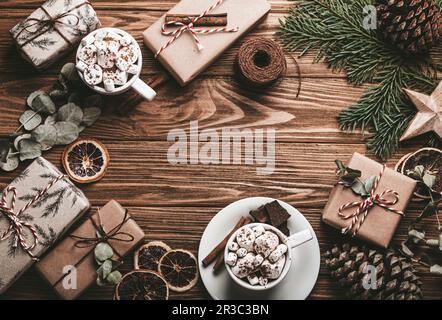 Christmas decorated background with wrapped presents, fir tree branch, marshmallow cacao cups on wooden table. Happy Xmas wrapping gift boxes top view Stock Photo