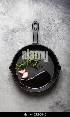 Black cast iron frying pan with oil, garlic, pepper and rosemary Stock Photo