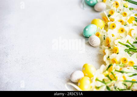 Holiday Easter frame made with daffodils and colored eggs on concrete background Stock Photo