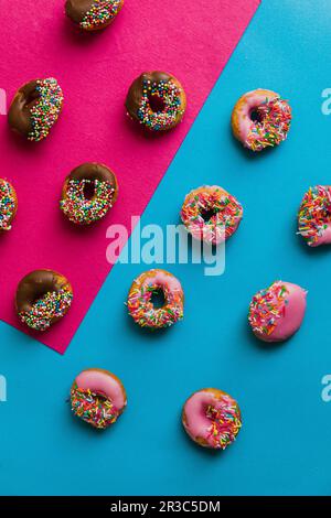 Donuts with icing and sugar sprinkles on a two-coloured base Stock Photo