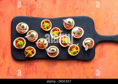 Tartelettes with mozzarella, pea puree, peppers, pesto, red onions and tomatoes Stock Photo