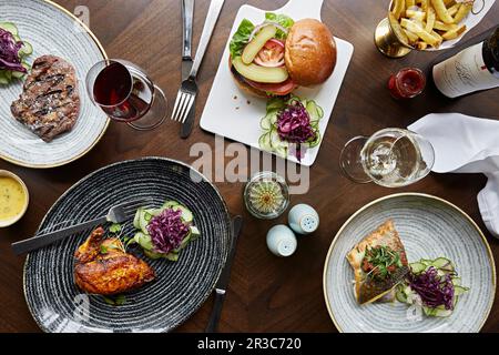 A selection of dishes, steak, chicken, sea bass and a beef burger with fries and wine Stock Photo
