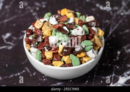 Colorful chocolate candy stones. Stone chocolate dragee in ceramic bowl on dark background. Small multi-colored candies. Close up Stock Photo