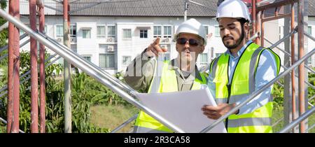 Two young architect discussion or contractor man while looking blueprint building structure together for survey on construction site, engineer plannin Stock Photo