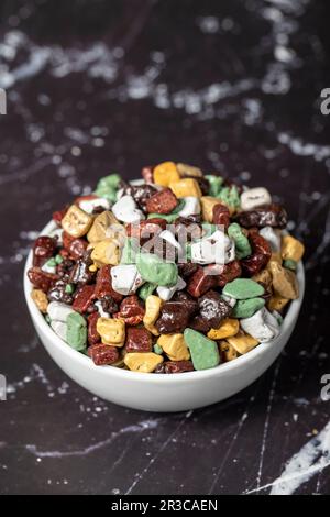 Colorful chocolate candy stones. Stone chocolate dragee in ceramic bowl on dark background. Small multi-colored candies. Close up Stock Photo