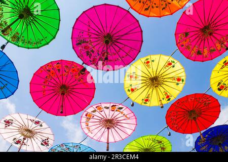 The colorful umbrellas hanging are seen from a lower perspective against a blue sky background Stock Photo